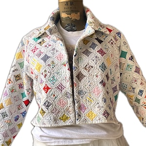 May include: A cropped, open-front jacket made from a patchwork quilt. The jacket features a diamond pattern with various colorful fabric squares. The collar and edges are finished with a white fabric. The jacket is displayed on a mannequin.