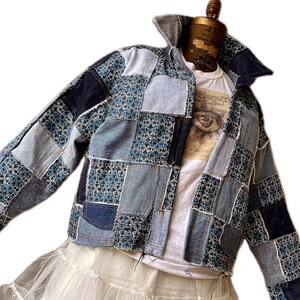 May include: A blue denim jacket with a patchwork design. The jacket is made of different shades of blue denim and has a white cotton lining. The jacket has a button-up closure and long sleeves.
