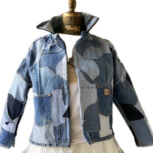 May include: A blue denim jacket made from patchwork pieces of denim. The jacket has a collar and long sleeves. The jacket is cropped and has a slightly oversized fit.