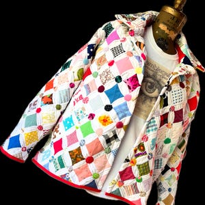 May include: A colorful patchwork jacket with a diamond pattern. The jacket features a variety of fabric patterns and colors, including red, pink, blue, and green. The edges are trimmed with red binding, and the jacket is displayed on a mannequin.