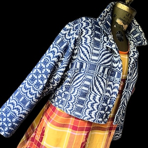 May include: A blue and white patterned jacket with a wide collar. The jacket is displayed on a mannequin. The jacket is paired with a yellow and red plaid dress. The background is black.