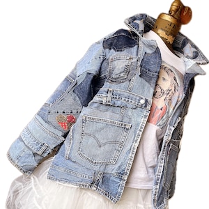 May include: A blue denim jacket with a patchwork design. The jacket has a variety of different denim fabrics sewn together, creating a unique and stylish look. The jacket has a button closure and two pockets on the front.