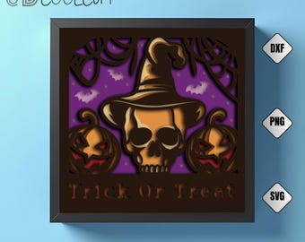 May include: A Halloween-themed shadow box with a skull wearing a witch hat, two jack-o'-lanterns, and the text "Trick or Treat." The background is purple with bats and spiderwebs. The frame is black, and the design is layered.