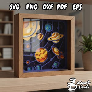 May include: A framed, layered paper art piece depicting a solar system with planets, a sun, and a rocket ship. The artwork is in a wooden frame and features the text "SVG PNG DXF PDF EPS" at the top and "3 Cool Cut" at the bottom.