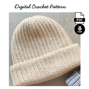 Puede incluir: Gorro de ganchillo color crema con borde acanalado. El gorro está hecho con un punto texturizado y presenta el texto "Digital Crochet Pattern" en la parte superior. Un icono de PDF y una flecha de descarga están en la esquina superior derecha.