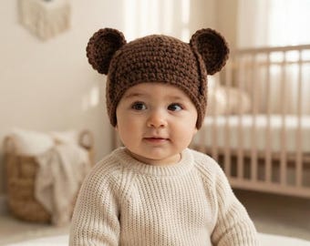 May include: A dark brown crochet beanie featuring two rounded bear ears on top. The hat is crafted with a textured yarn stitch pattern and fits snugly around the head, providing a simple and functional design for headwear.