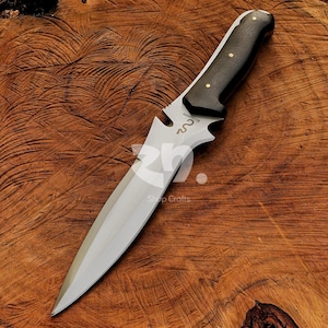 May include: A hunting knife with a polished steel blade and a dark wooden handle. The handle is secured with brass rivets. The knife has a decorative cutout near the blade and is set against a wooden background.