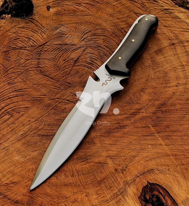 May include: A hunting knife with a polished steel blade and a dark wooden handle. The handle is secured with brass rivets. The knife has a decorative cutout near the blade and is set against a wooden background.