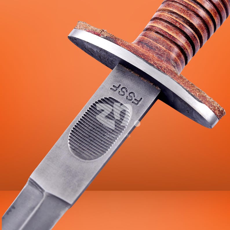 May include: A combat knife featuring a double-edged steel blade with a textured thumb grip area and the letters FSSF stamped near the crossguard. The handle is constructed from stacked brown leather rings with a metallic guard and pommel.