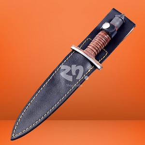 May include: A fixed-blade knife with a brown leather-wrapped handle and a silver-toned metal guard, housed in a black leather sheath featuring yellow contrast stitching and a snap button closure. The logo "rn" is visible on the sheath surface.