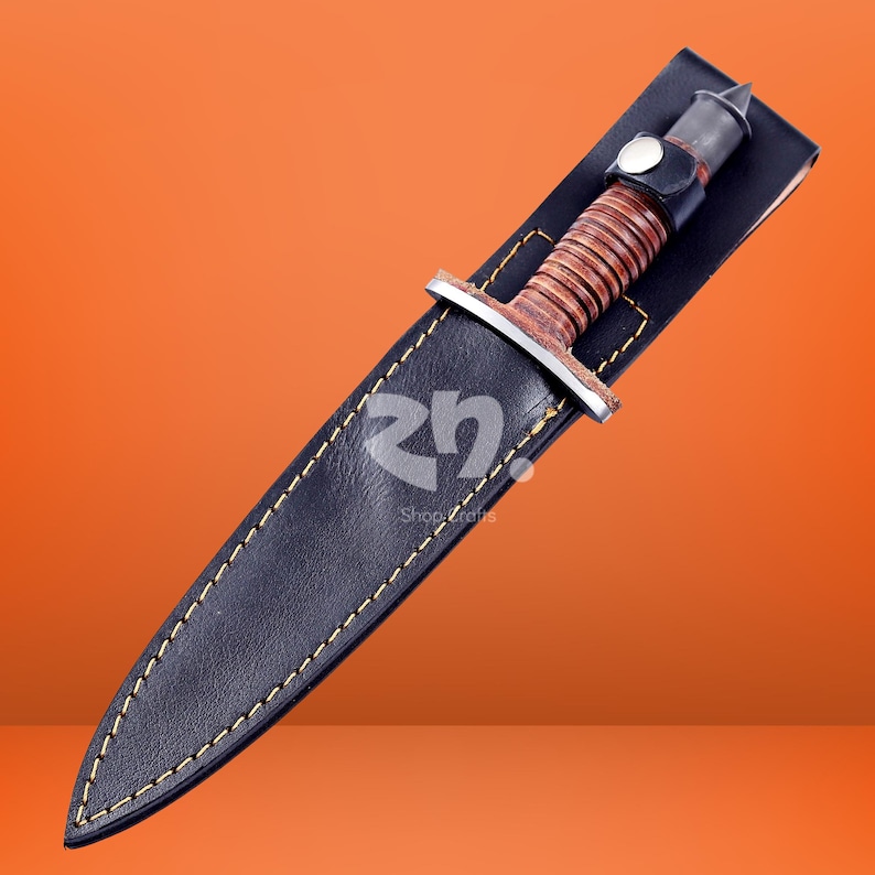 May include: A fixed-blade knife with a brown leather-wrapped handle and a silver-toned metal guard, housed in a black leather sheath featuring yellow contrast stitching and a snap button closure. The logo "rn" is visible on the sheath surface.