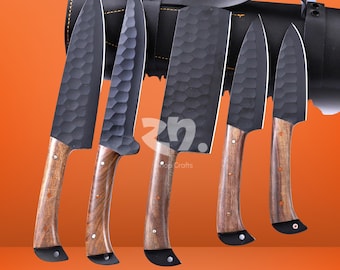 May include: A set of five kitchen knives with black blades and wooden handles. The blades have a textured surface. The knives are displayed with a black leather carrying case. The handles are a light brown color.