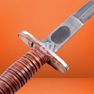 May include: A combat knife featuring a brown leather-wrapped handle with horizontal ridges, a silver metal crossguard, and a steel blade. The blade is stamped with the letters FSSF above an oval-shaped textured grip area near the hilt.