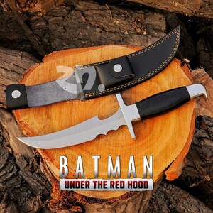 May include: A stainless steel knife with a black handle and a leather sheath. The blade has a unique serrated edge. The text "BATMAN UNDER THE RED HOOD" is displayed below the knife.