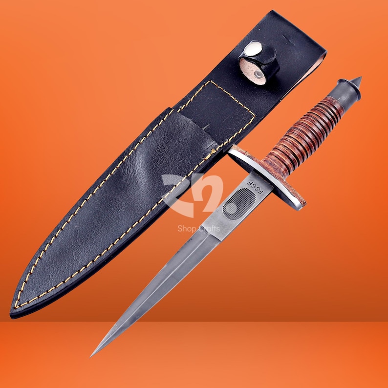 May include: A double-edged dagger with a pointed steel blade, a ribbed brown leather handle, and a metal crossguard marked with the text FSSF. The dagger is accompanied by a black leather sheath featuring yellow stitching and a snap button closure.
