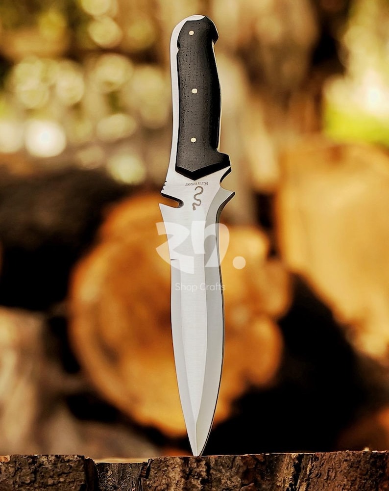 May include: A stainless steel knife with a black handle and a silver blade. The handle has three white dots and a decorative design near the blade. The text "Shop Crafts" is visible.