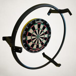 Może przedstawiać: Czarna tarcza do darta z systemem montażowym. Tarcza ma czarne tło z czerwonymi, zielonymi i białymi sekcjami. System montażowy to czarna metalowa rama o okrągłym kształcie. Widoczny jest tekst "WINMAU MASTERS PRO".