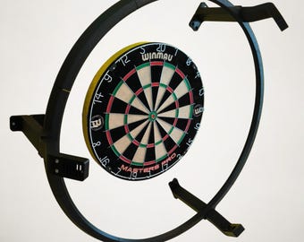 Può includere: Un bersaglio per freccette nero con sistema di montaggio. Il bersaglio ha uno sfondo nero con sezioni rosse, verdi e bianche. Il sistema di montaggio è un telaio in metallo nero con un design circolare. Il testo "WINMAU MASTERS PRO" è visibile.