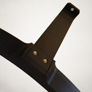 K&ouml;nnte beinhalten: Eine schwarze, abgewinkelte Komponente mit dem Text "Variante 3" in der oberen linken Ecke. Die Komponente besteht aus einem mattschwarzen Material und wird mit silbernen Schrauben zusammengehalten. Das Design scheint Teil einer gr&ouml;&szlig;eren Struktur zu sein.