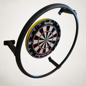K&ouml;nnte beinhalten: Ein schwarzer Dartscheibenrahmen aus Metall mit einer Winmau Dartscheibe. Die Dartscheibe hat ein Farbschema in Schwarz, Rot, Gelb und Wei&szlig;. Der Text "Variante 3" befindet sich oben links. Die Dartscheibe ist an einer Wand befestigt.
