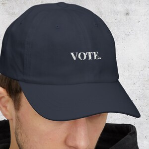 May include: Navy blue baseball cap with the word "VOTE" embroidered in white. The cap has a curved brim and a classic, adjustable design. A simple yet impactful accessory.