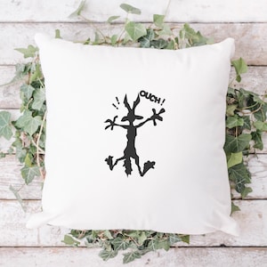 May include: White cushion with a black silhouette of a cartoon coyote with the word "OUCH!" above it.