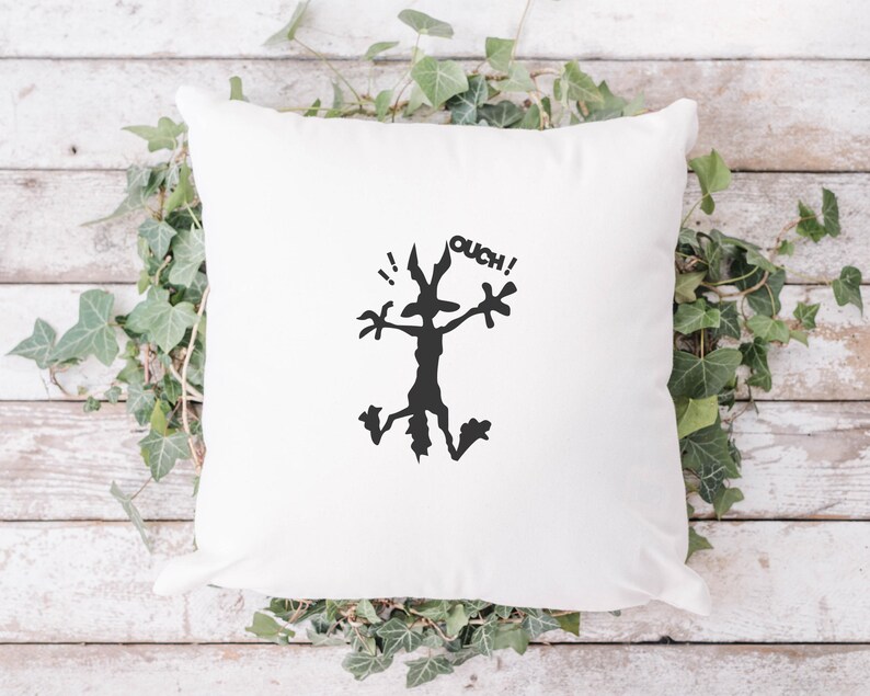 May include: White cushion with a black silhouette of a cartoon coyote with the word "OUCH!" above it.