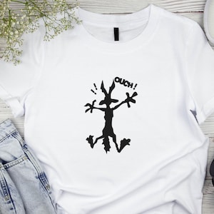 May include: White t-shirt featuring a black silhouette of a cartoon coyote with the word "OUCH!" above it.