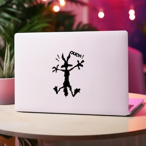 May include: A white laptop with a black silhouette of a cartoon character with the word "ouch!" above it.