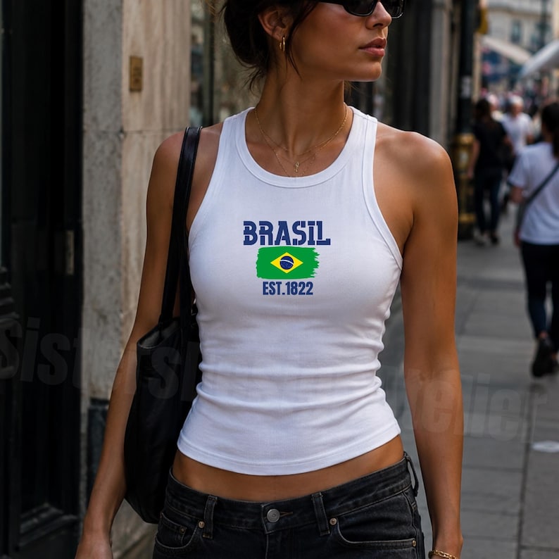 May include: A white sleeveless tank top featuring a graphic print on the chest. The print includes the word BRASIL in blue, a green, yellow, and blue Brazilian flag design, and the text EST.1822 in blue. The tank top has a ribbed crew neckline.