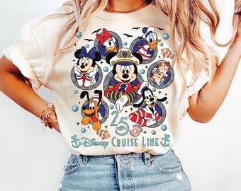 Pode incluir: Camiseta creme com um gráfico colorido de personagens da Disney em designs de vigias. O design inclui Mickey Mouse, Minnie Mouse, Pato Donald, Margarida, Pateta, Pluto e Tico e Teco. O texto "25 Disney Cruise Line" também está presente.