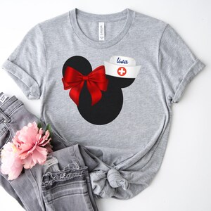 May include: Gray t-shirt with a black and red Mickey Mouse design. The Mickey Mouse has a red bow and a white nurse's hat with a red cross and the name "Lisa" written on it.