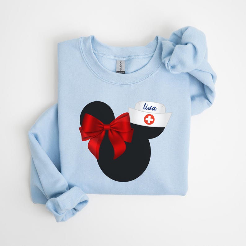 May include: Light blue sweatshirt with a black and red Mickey Mouse design. The Mickey Mouse has a red bow and a white nurse's hat with a red cross and the name "Lisa" on it.