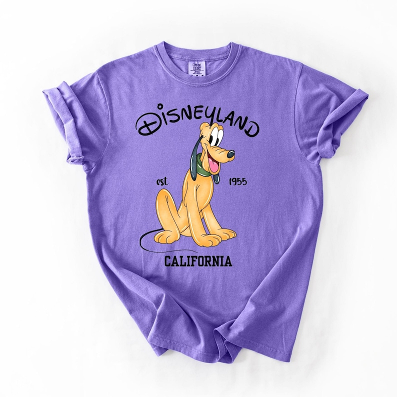 Peut inclure: T-shirt lilas avec un dessin de Pluto, personnage Disney. Le logo Disneyland et le texte "est 1955 CALIFORNIA" sont imprim&eacute;s en noir. Un v&ecirc;tement sur le th&egrave;me de Disney.