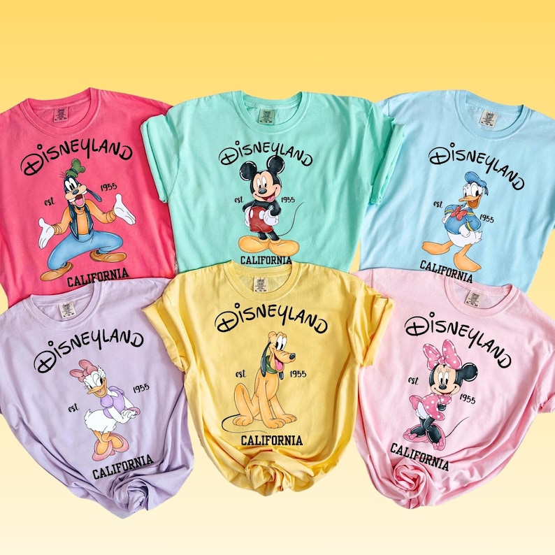 Peut inclure: Six t-shirts color&eacute;s avec des motifs Disneyland. Chaque t-shirt affiche le logo Disneyland, l'ann&eacute;e 1955 et le mot "California". Les chemises pr&eacute;sentent divers personnages Disney, dont Mickey Mouse, Dingo, Donald Duck et Minnie Mouse.