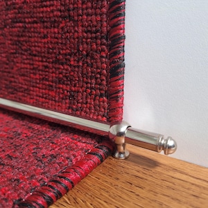 May include: Close-up of a red and black stair tread with a silver metal rod and end cap. The rod is used to secure the stair tread in place.