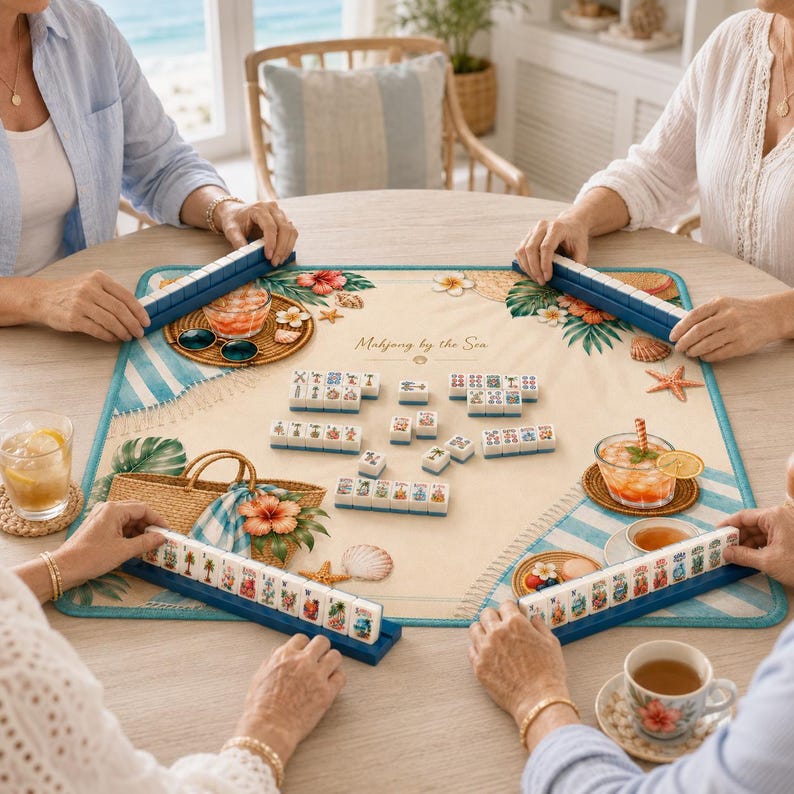 Puede incluir: Un juego de Mahjong sobre un tapete con tem&aacute;tica de playa con el texto "Mahjong by the Sea". El tapete presenta un borde a rayas azules y blancas, detalles florales y una bolsa de paja. El juego est&aacute; configurado con fichas y estantes azules.