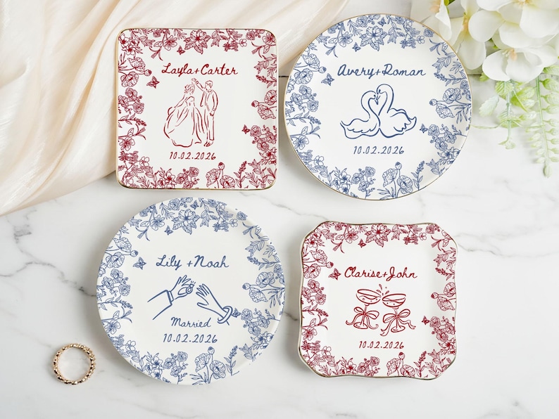 May include: Four decorative plates with floral borders and gold rims. Each plate features a unique design in red or blue, including illustrations of a couple, swans, hands, and champagne glasses. The plates are personalized with names and a date.