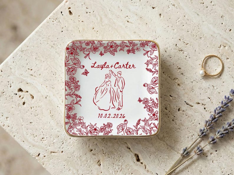 May include: Square white ceramic ring dish with a red floral border and a red illustration of a couple dancing. The dish has gold trim and the names "Layla + Carter" and the date "10.02.2026" are printed on the dish.