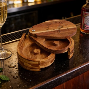 Könnte beinhalten: Ein tropfenförmiges Bar-Tablett aus Holz mit einem Klappdeckel. Der Deckel ist mit dem Namen "MARIA JOHNSON" und dem Wort "bartender" graviert. Das Tablett ist aus hellbraunem Holz gefertigt und steht auf einer dunklen Oberfläche.