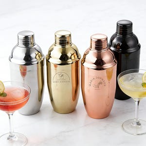 May include: Four cocktail shakers in silver, gold, copper, and black, each with a stainless steel lid. The gold and copper shakers have custom text and a logo. Two cocktails are in the foreground.