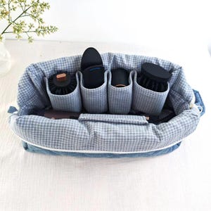 May include: A quilted blue denim storage bag with a white zipper and a light blue and white grid patterned interior lining. The bag features four internal fabric compartments designed to hold various hair styling tools and accessories securely.