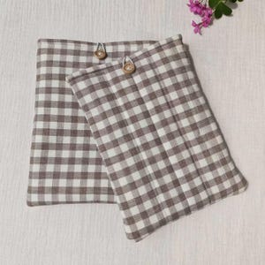 May include: Two rectangular fabric pouches featuring a brown and white gingham check pattern. Each pouch is constructed with a quilted texture and is secured at the top center with a single round, light-colored wooden button closure.