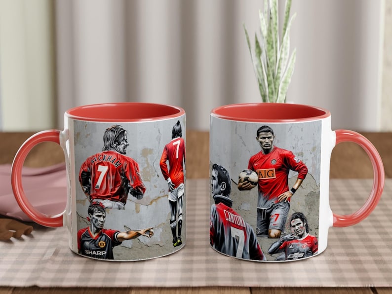 May include: Two red and white ceramic mugs with images of famous soccer players. The mugs feature images of David Beckham, Cristiano Ronaldo, Wayne Rooney, and Ryan Giggs. The mugs have red handles and red rims.
