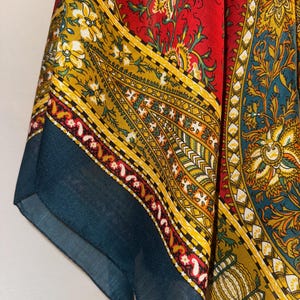 May include: A vibrant, patterned textile featuring a rich color palette. The design incorporates a red background with yellow, teal, and white floral and geometric patterns. The fabric has a flowing drape, suggesting it could be a scarf or shawl.