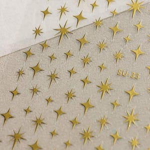 May include: A sheet of clear adhesive paper with gold glitter stars printed on it. The sheet is labeled "SU 33".