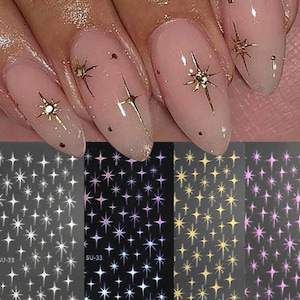 May include: Three sheets of nail art stickers with different designs. The first sheet has white star stickers, the second sheet has iridescent star stickers, and the third sheet has gold star stickers.