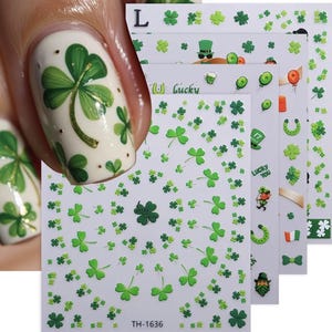 May include: Nail art stickers with St. Patrick's Day designs. The stickers feature green shamrocks, four-leaf clovers, and other festive elements. The stickers are on a white background, with some designs featuring gold accents. The image also shows a painted nail with a shamrock design.
