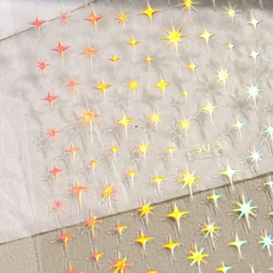 May include: A sheet of iridescent star stickers with a holographic finish. The stickers are arranged in rows and are perfect for adding a touch of sparkle to any project.