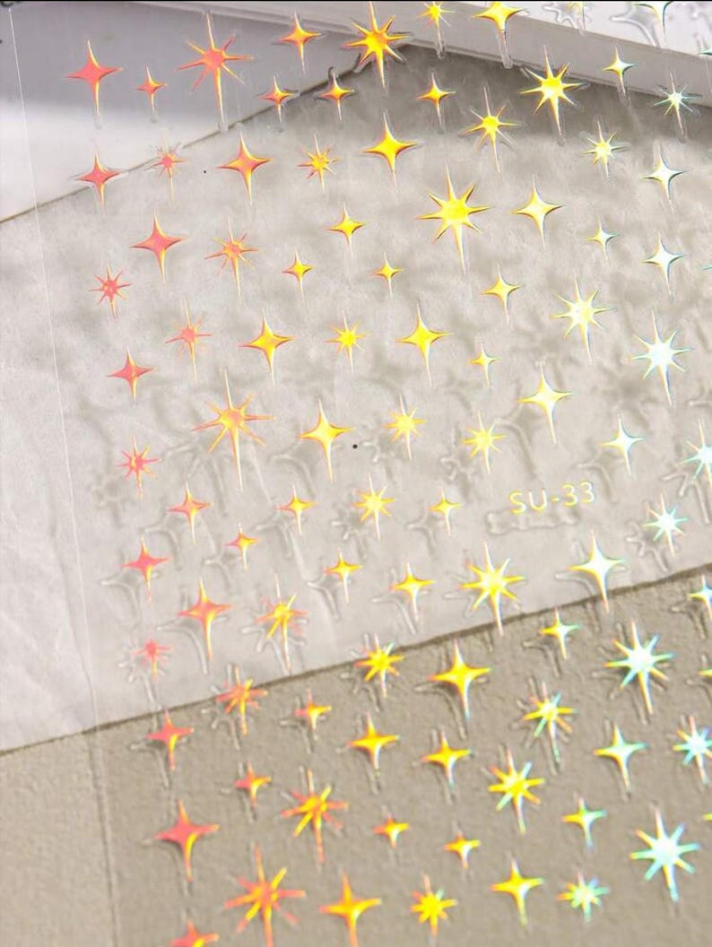 May include: A sheet of iridescent star stickers with a holographic finish. The stickers are arranged in rows and are perfect for adding a touch of sparkle to any project.